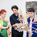 Three Asian people staring at a sculpture resembling a small wooden tree.