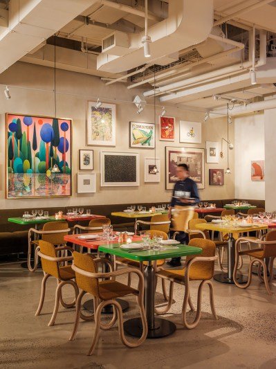 An extravagent, trendy dining room with a sprawling sculpture of mushroom-shaped lamps. In the background, a dozen artworks are hung on the wall, salon-style.