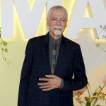 A man in a suit in front of the MoMA logo.