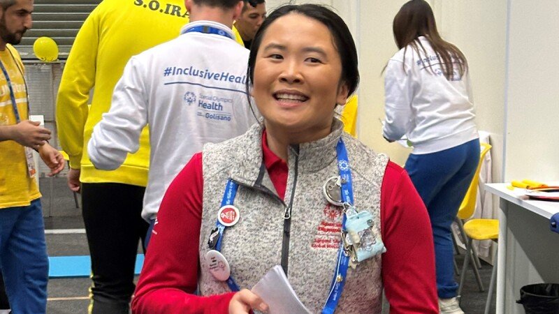 Young woman in a red shirt and light gray vest smiling and speaking.