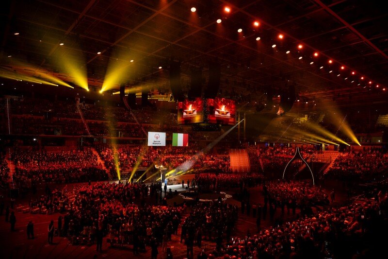 A stadium full of people at the Opening-Ceremony for the Special Olympics World Winter Games Turin 2025; a light show and video show are happening as athletes come into the arena.