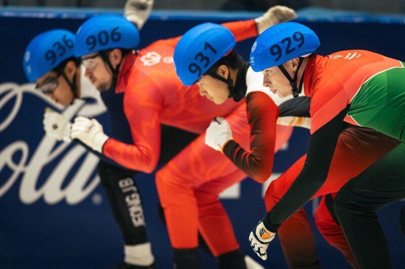 A speed skater competes in a speed skating race at an ice rink. Beside him are three other speed skating athletes